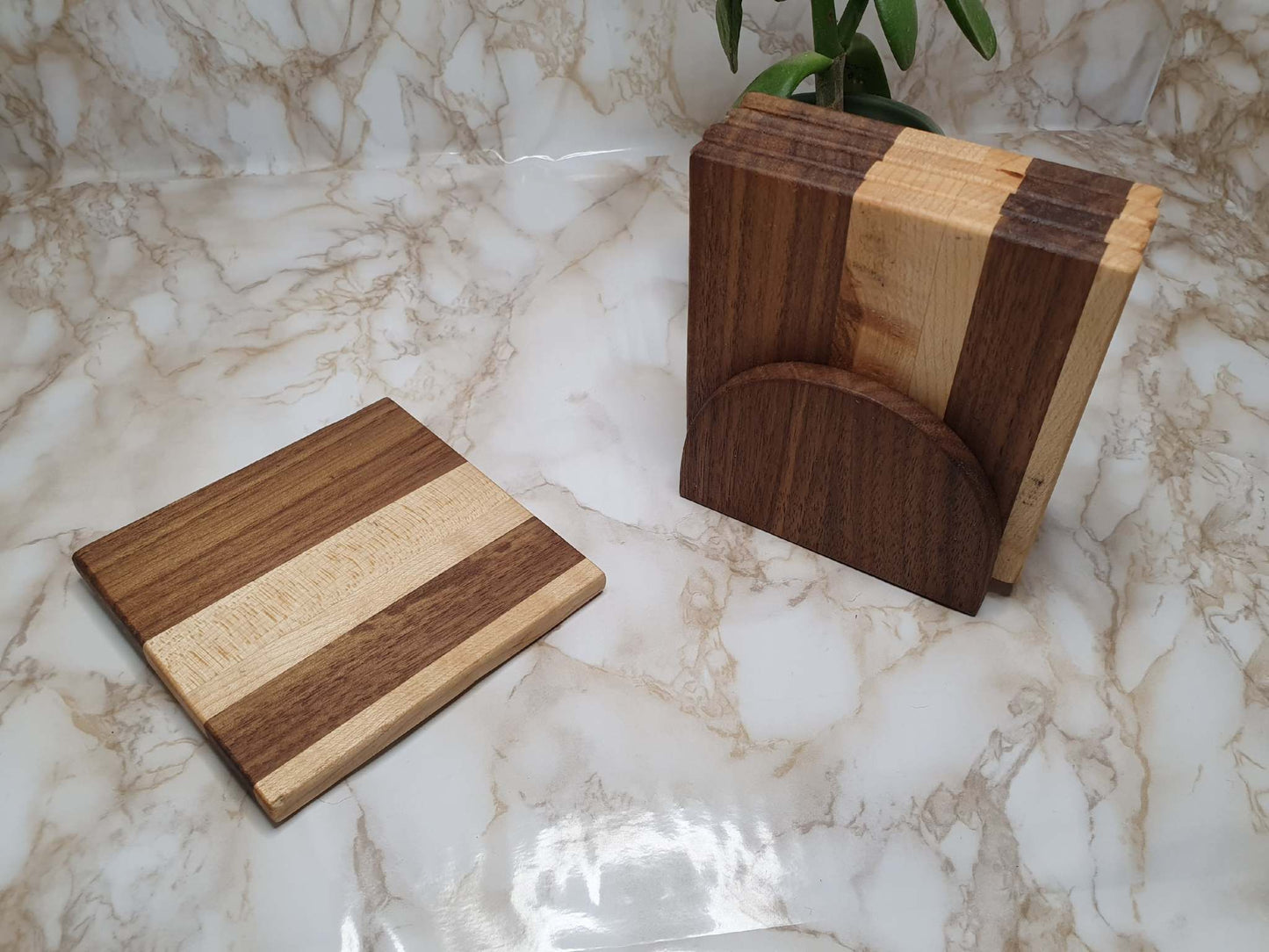 Set of 4 walnut and maple coasters with holder displayed on a marble surface.