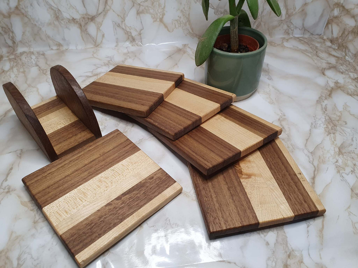 Set of 4 handmade walnut and maple coasters with holder on marble background.