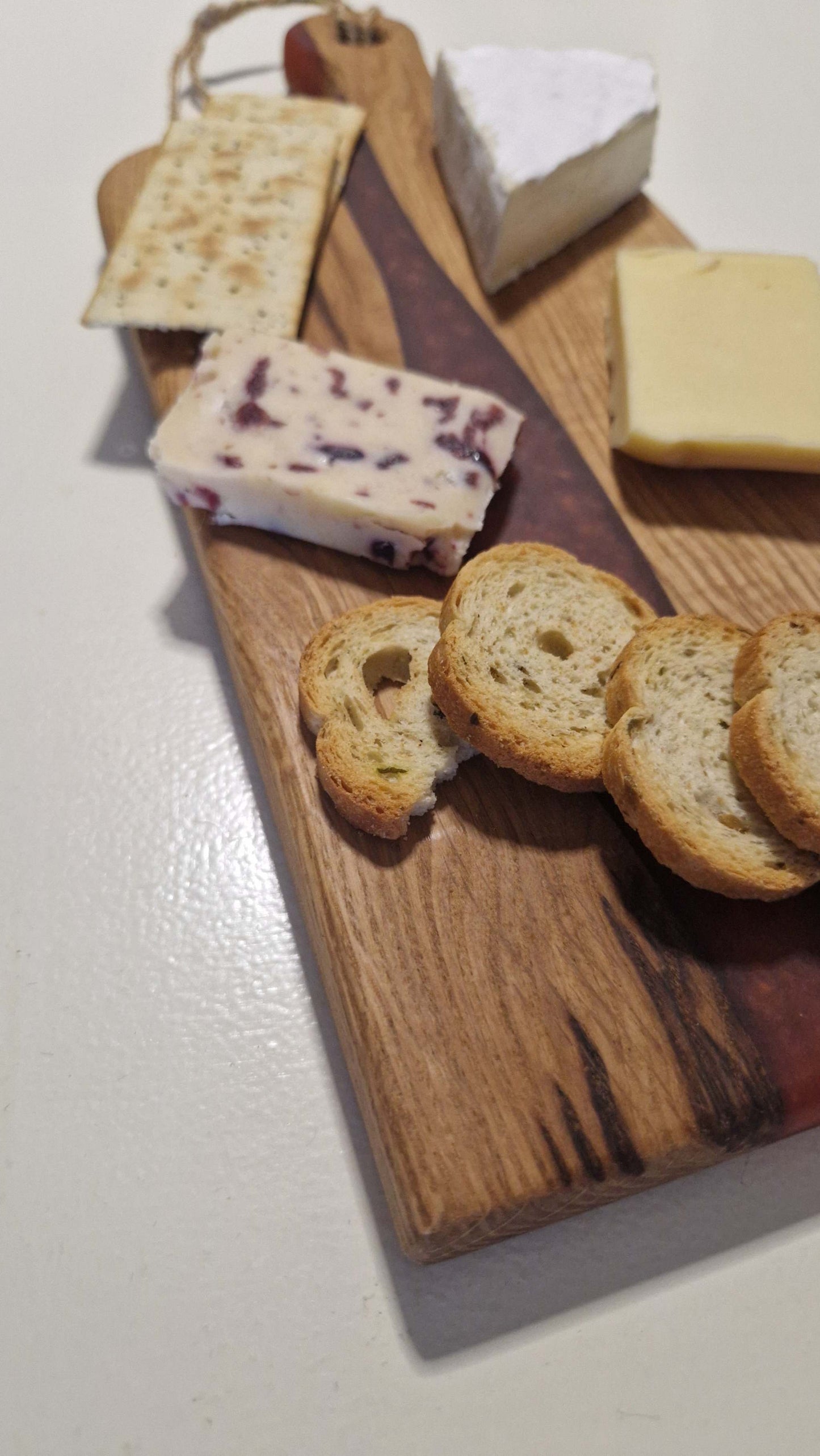 Handmade oak charcuterie board with red epoxy, featuring assorted cheeses and crackers.