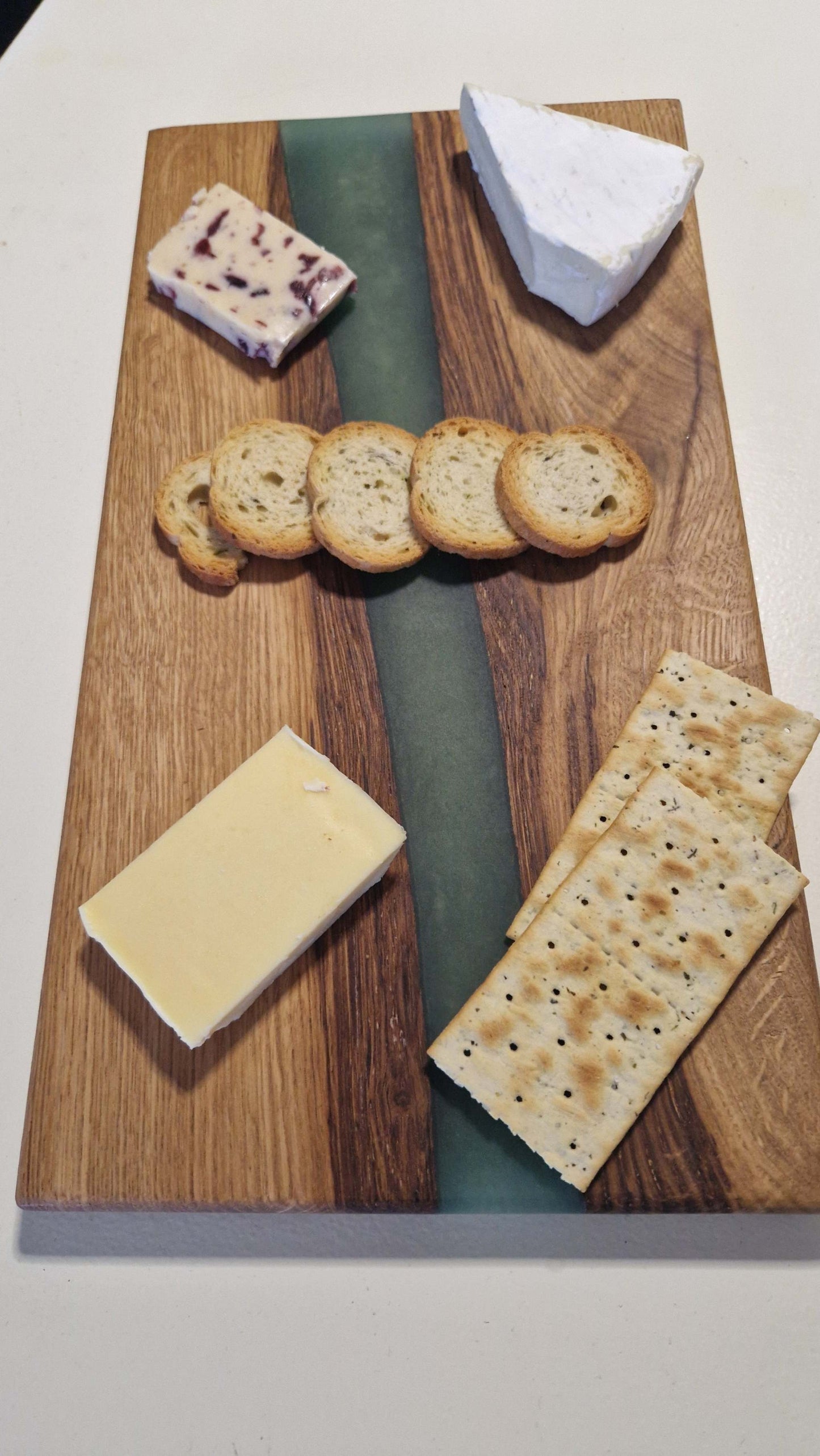 Handmade charcuterie board with green epoxy in oak wood, featuring assorted cheeses and crackers.