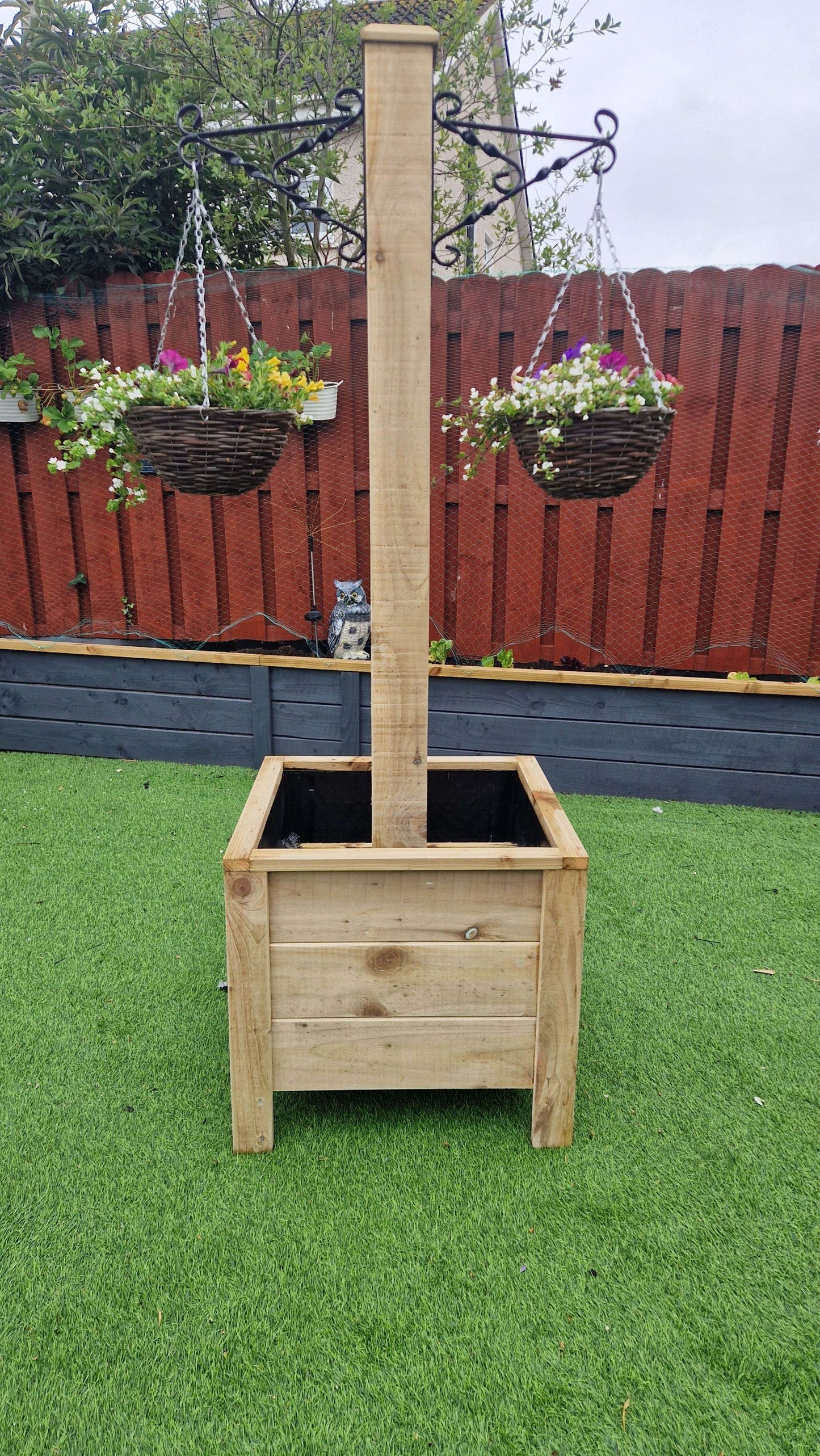Handcrafted wooden planter with integrated hanging basket pole on a green garden lawn.