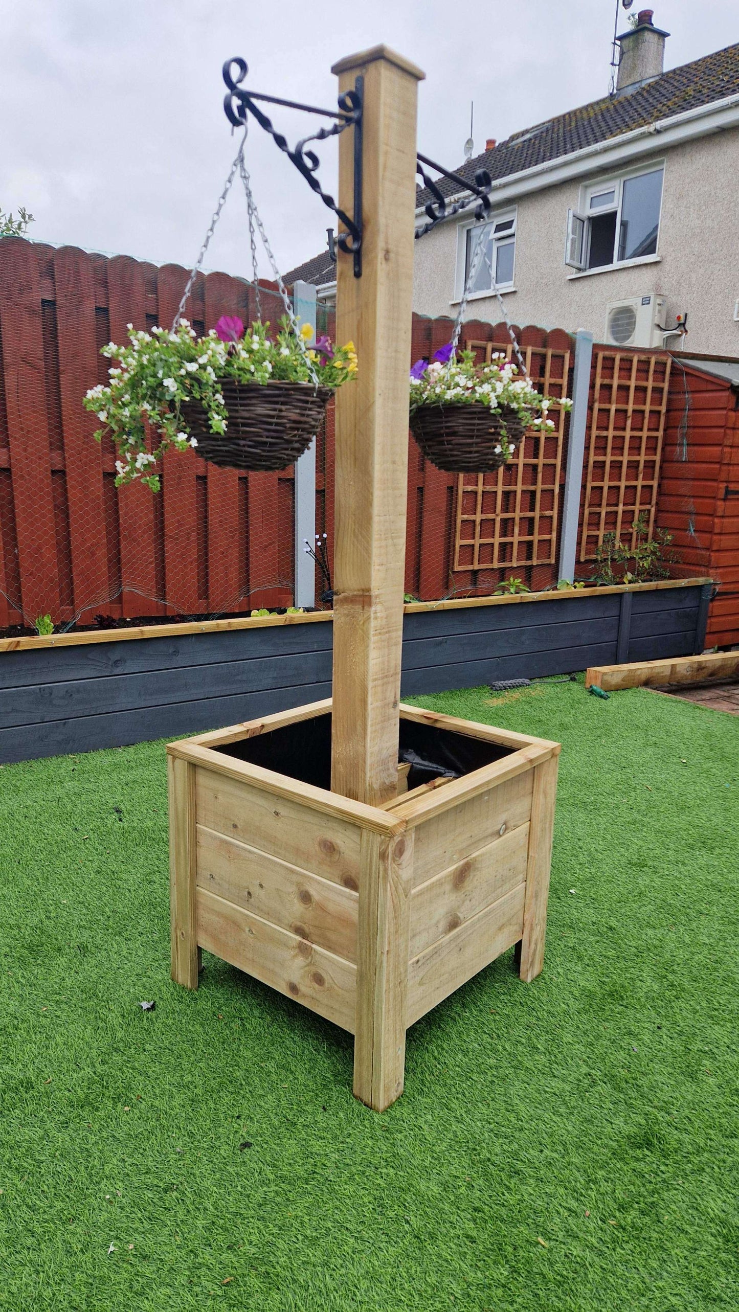 Handcrafted wooden planter with integrated hanging basket pole on a green garden lawn.