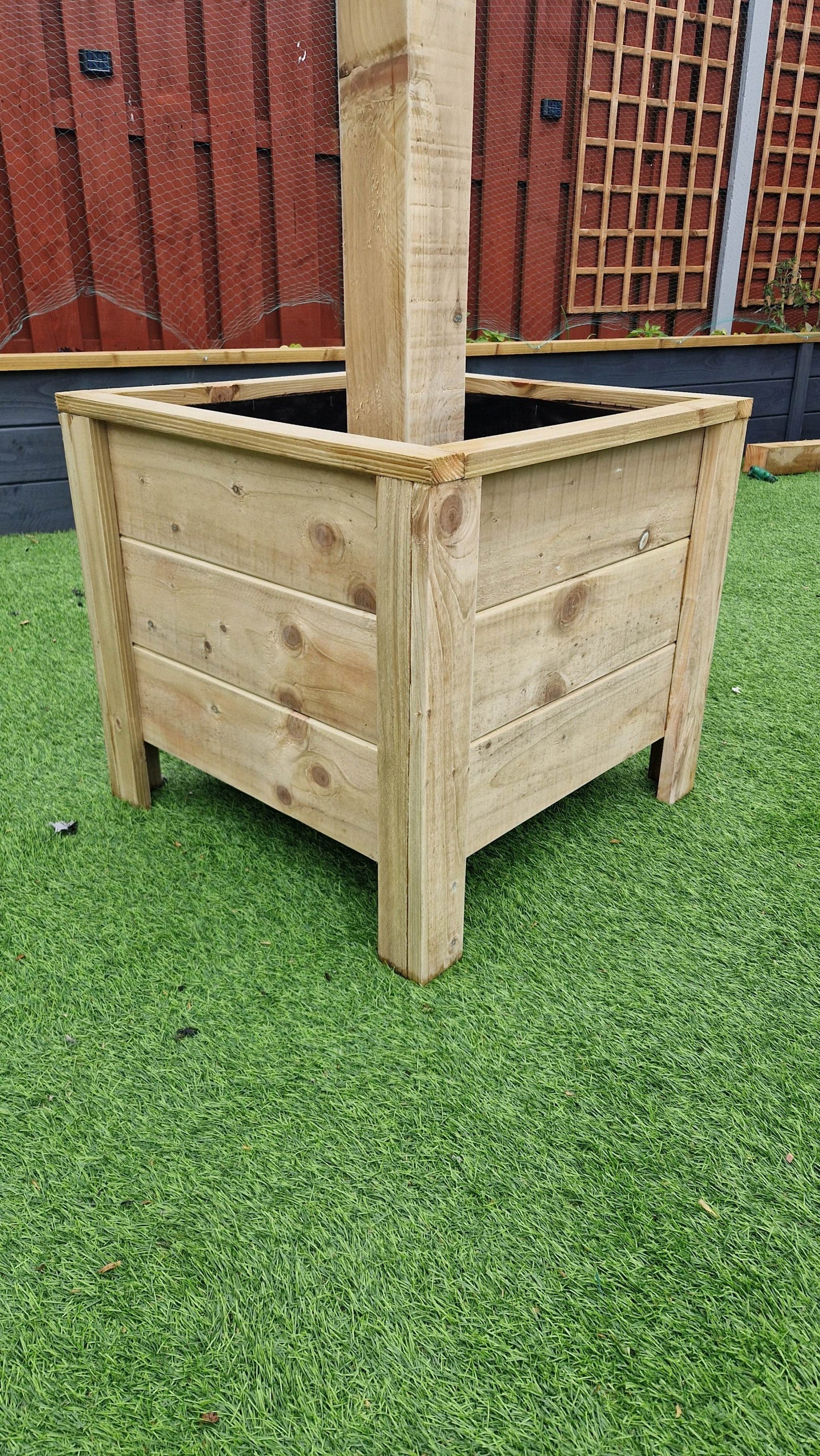 Handcrafted wooden planter with integrated hanging basket pole on a green garden lawn.