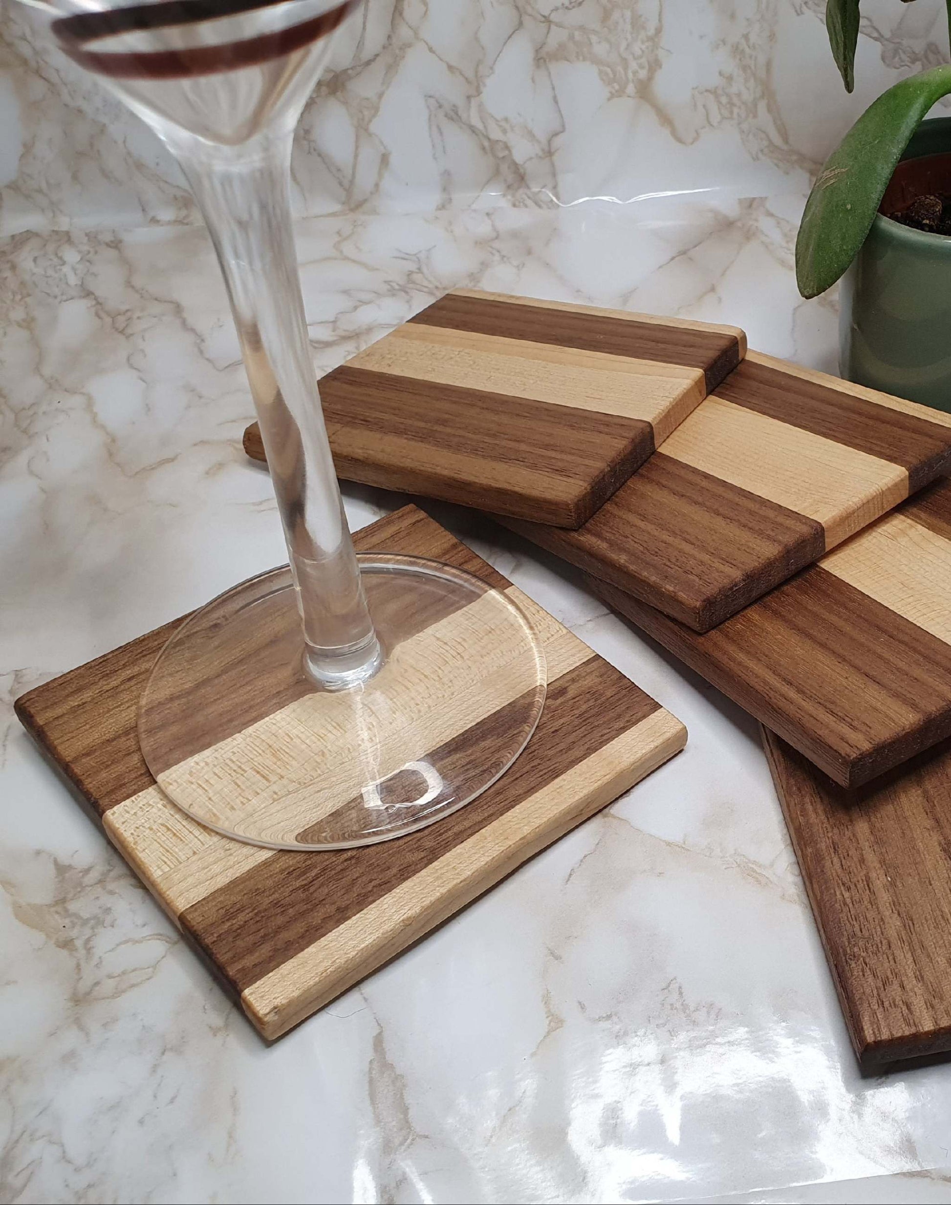 Set of 4 elegant maple and walnut coasters with holder on marble table, wine glass on top.