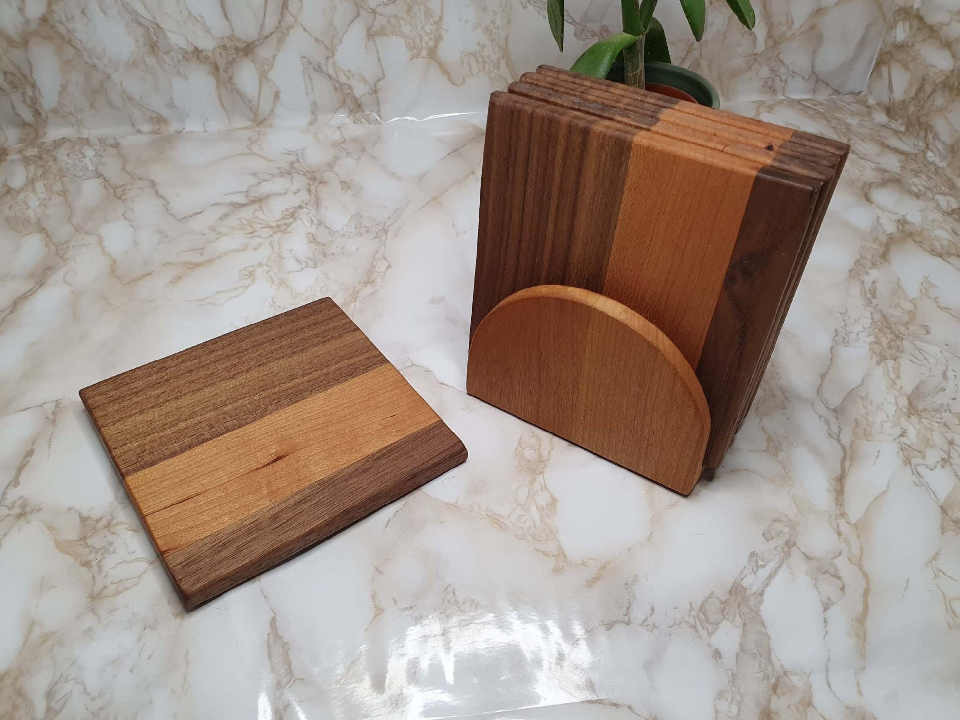 Set of 4 coasters with holder in walnut and cherry wood on marble background.