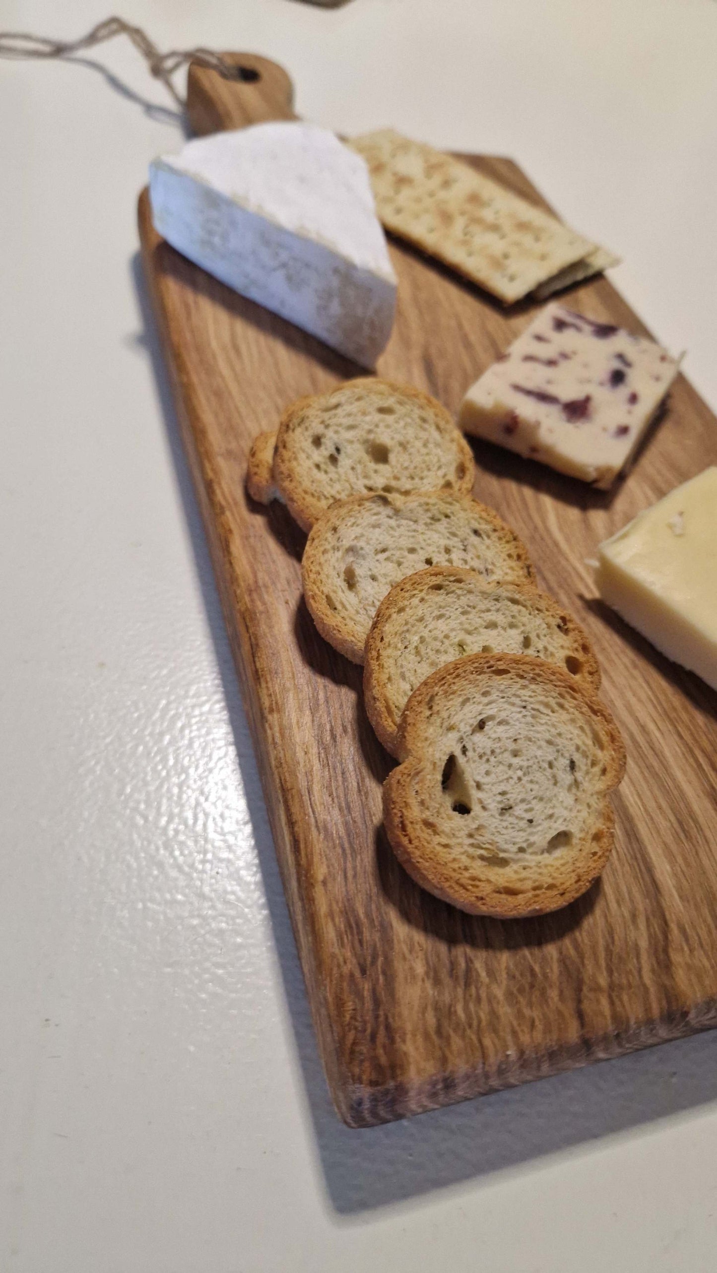 Handmade oak charcuterie board with assorted cheeses and bread slices.