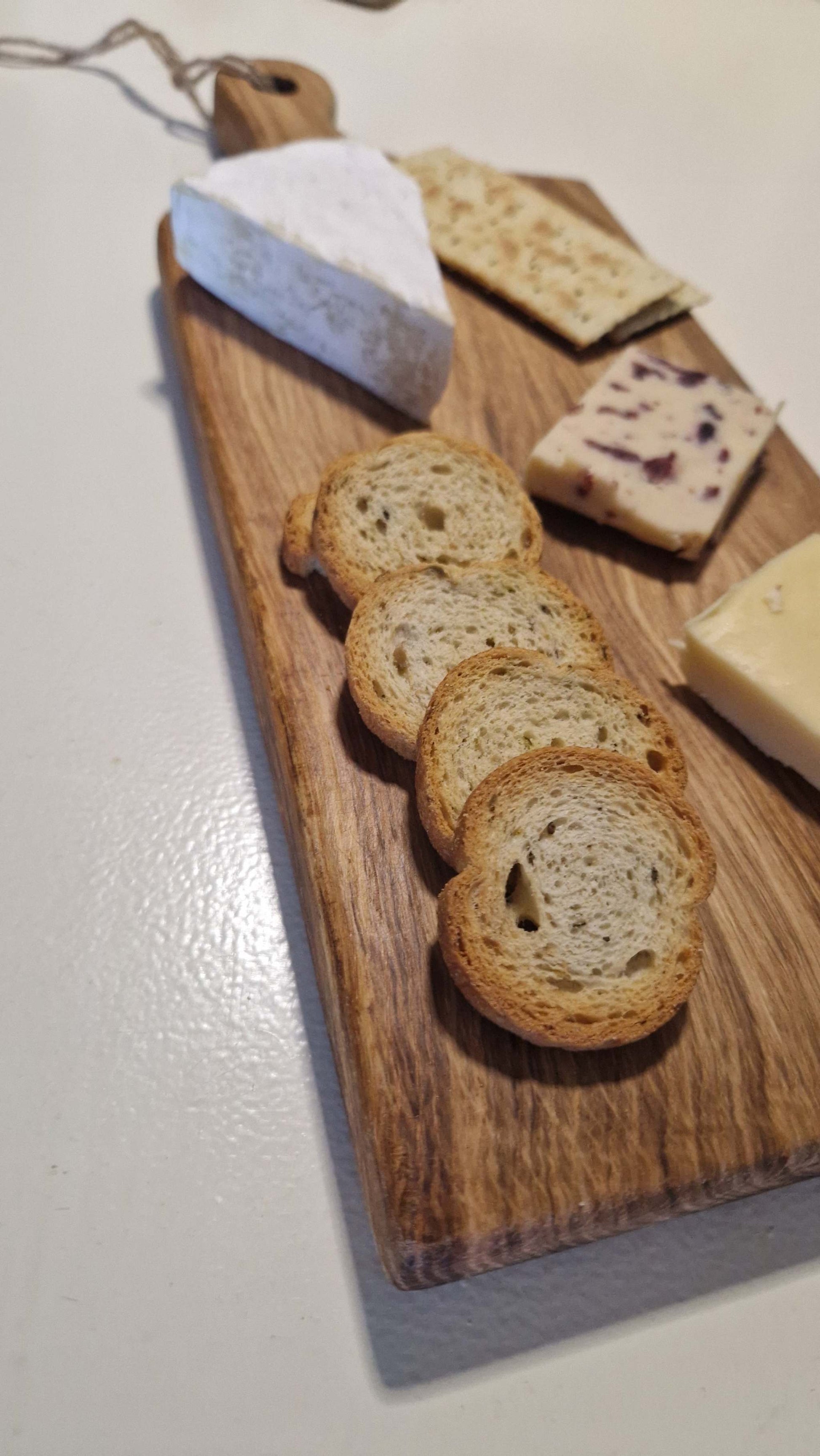 Handmade oak charcuterie board with assorted cheeses and bread slices.