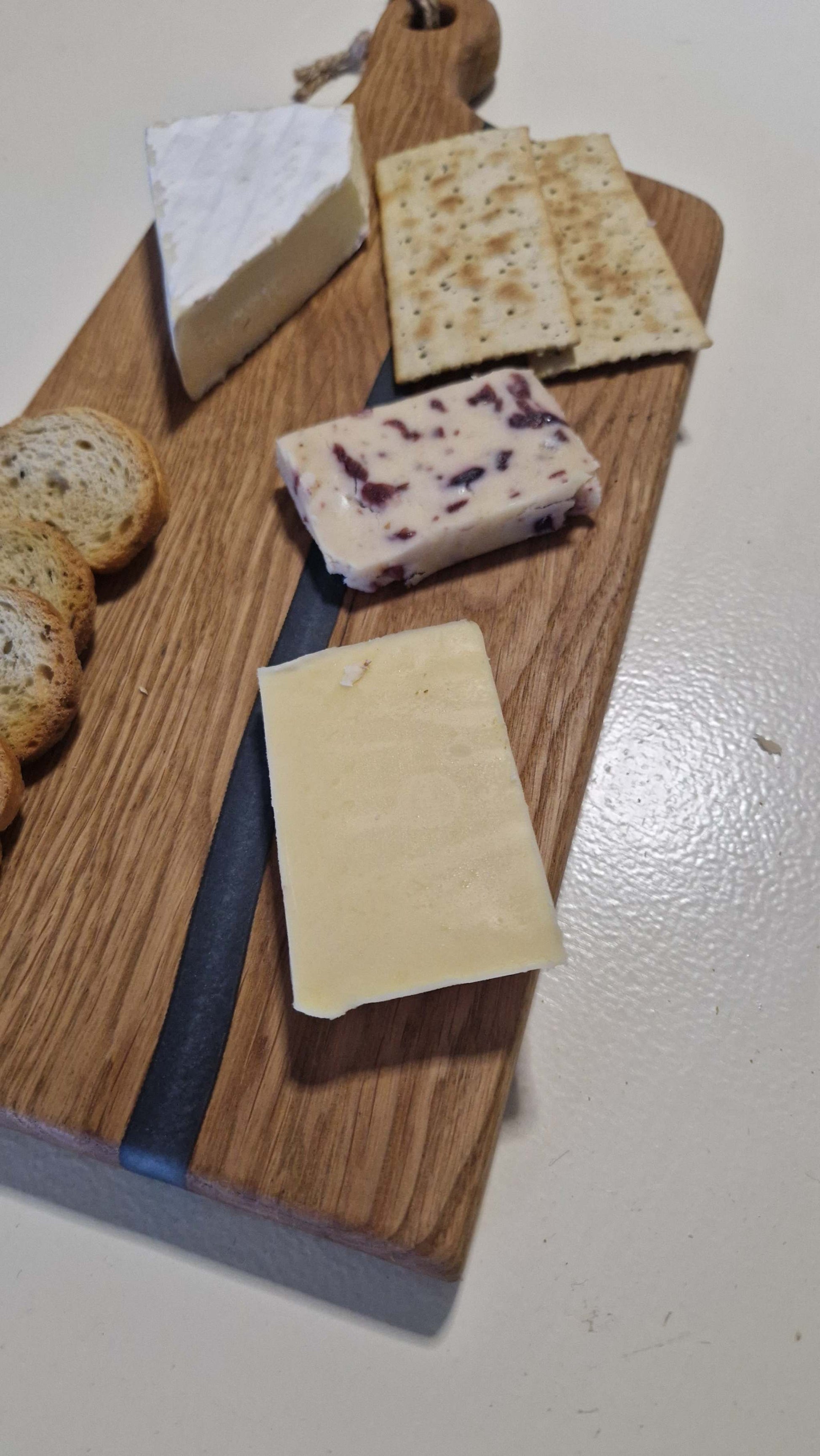 Handmade oak charcuterie board with grey epoxy, featuring cheeses and crackers.