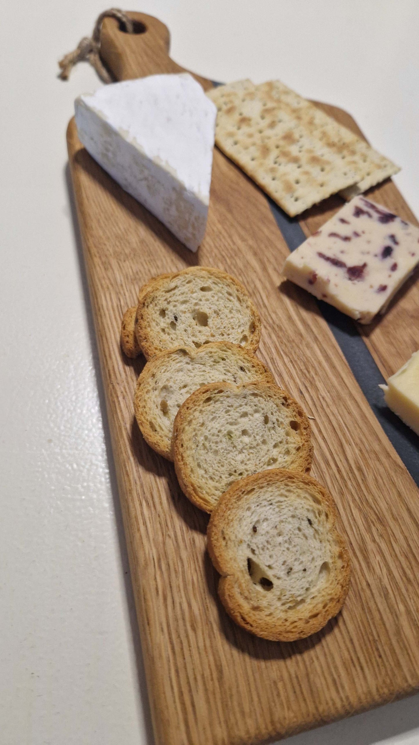Handmade oak charcuterie board with grey epoxy, serving cheese and crackers.