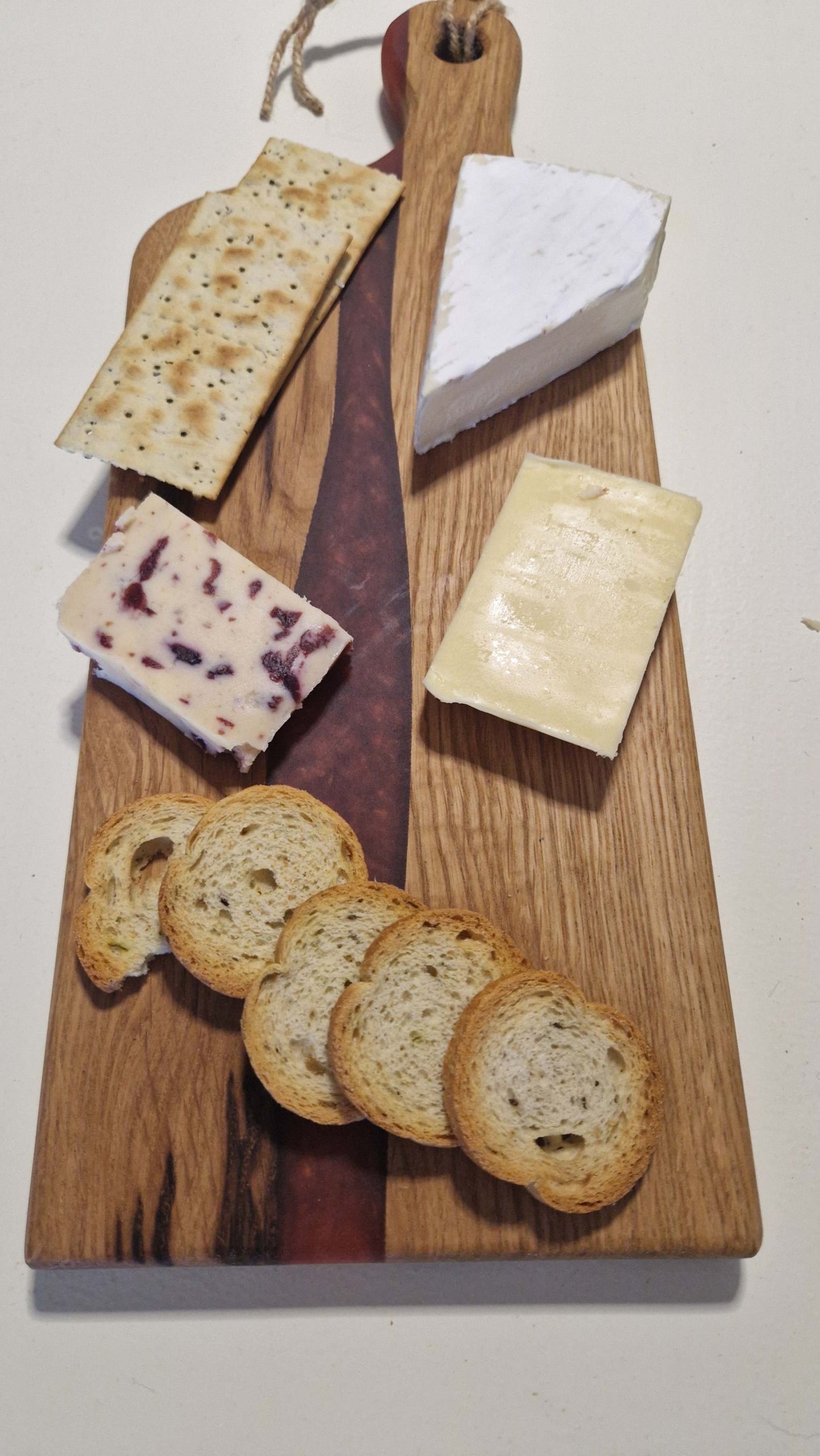 Handmade oak charcuterie board with red epoxy, featuring assorted cheeses and crackers.