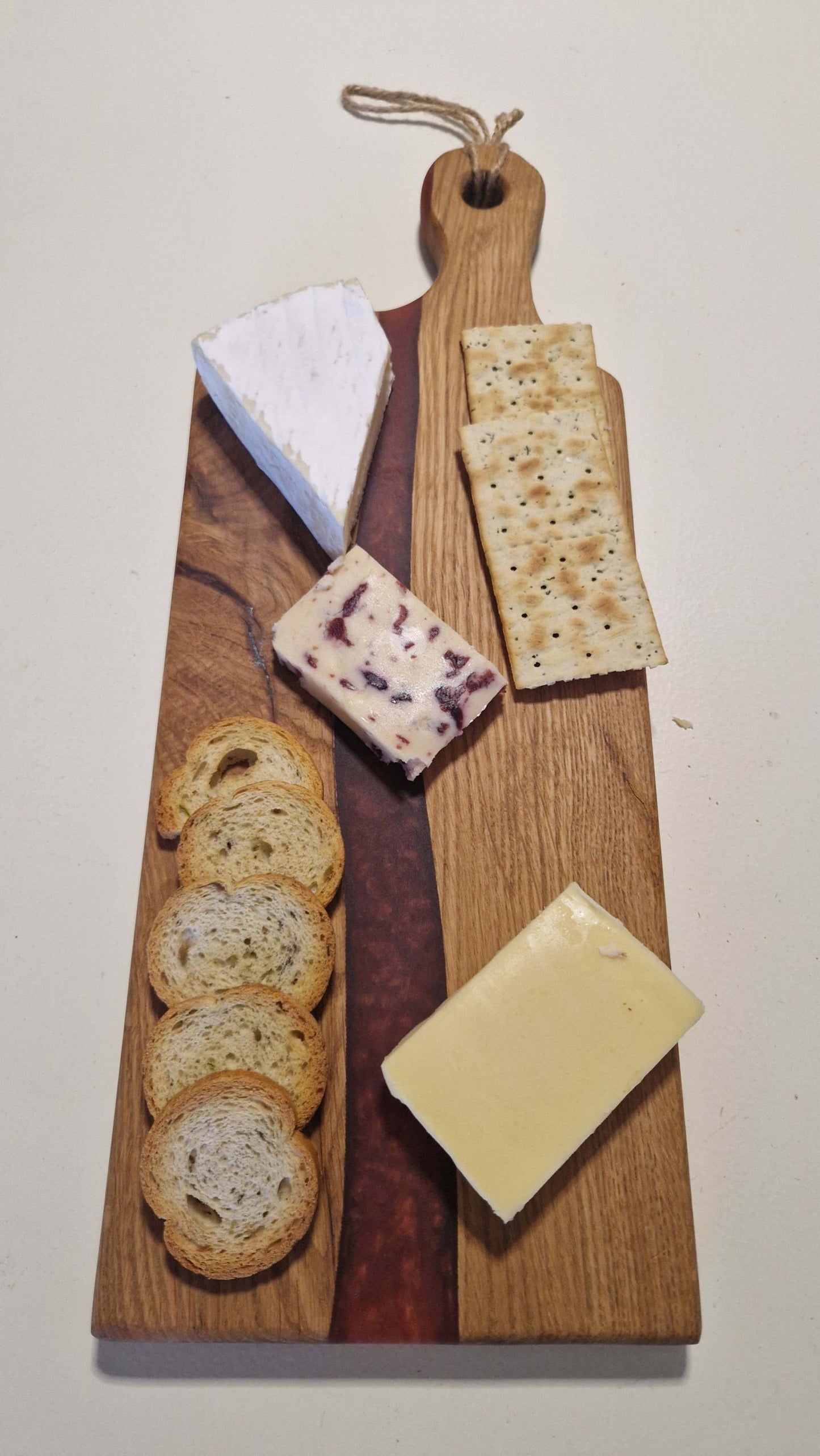Handmade charcuterie board in oak with red epoxy, featuring various cheeses and crackers.