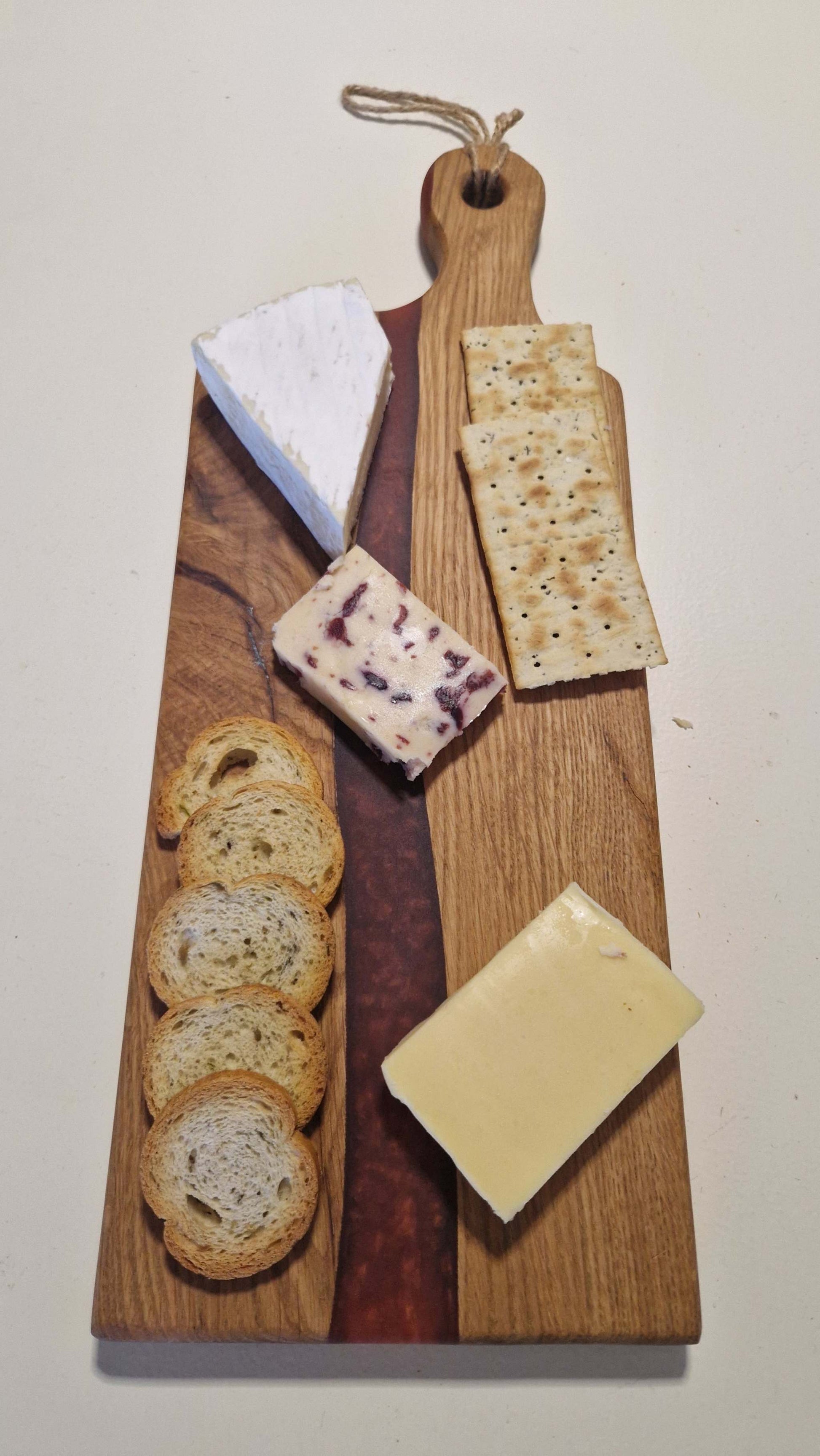 Handmade charcuterie board in oak with red epoxy, featuring various cheeses and crackers.