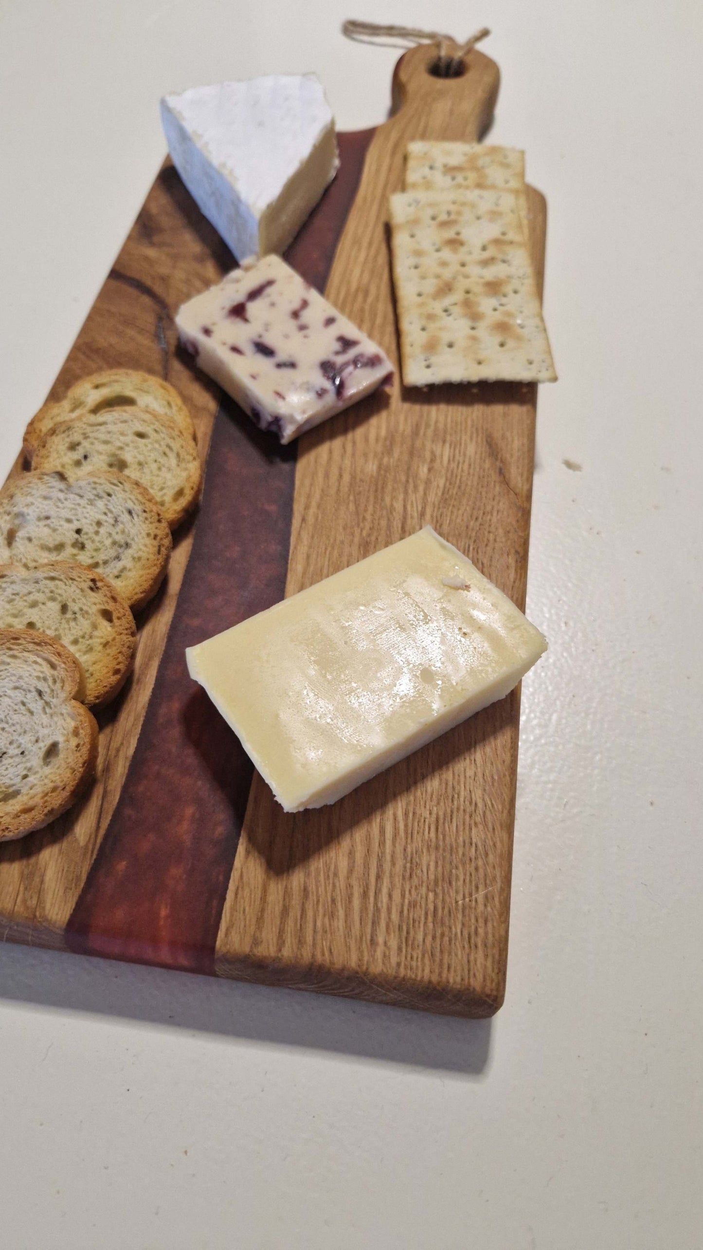 Handmade charcuterie board with red epoxy, showcasing cheese and crackers.