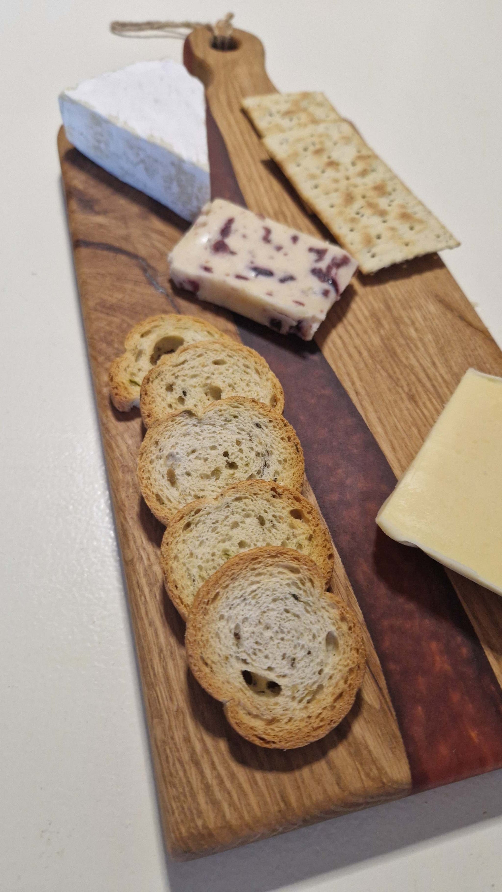 Handmade oak charcuterie board with red epoxy, featuring cheese and crackers.