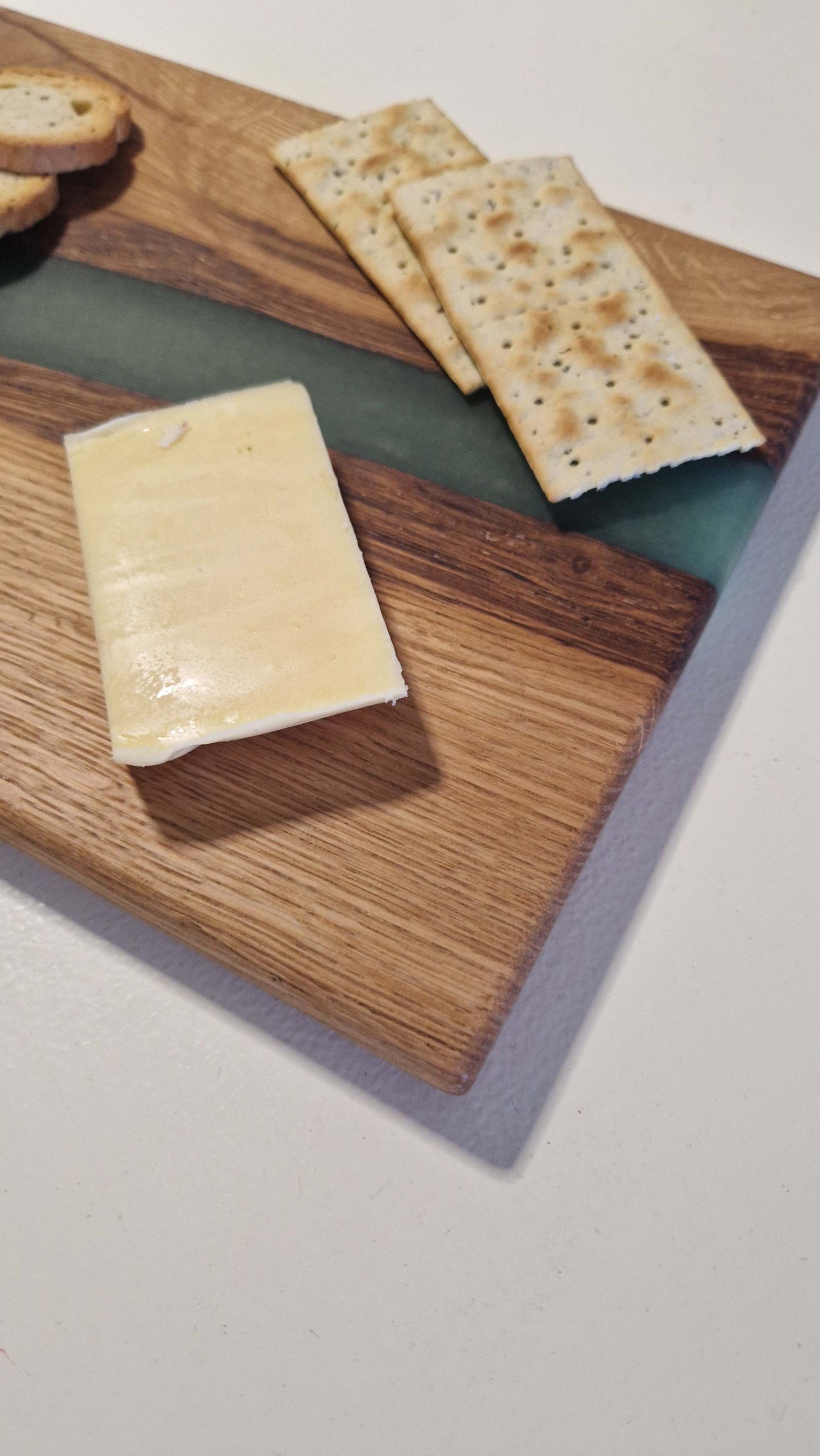 Handmade oak charcuterie board with green epoxy, featuring cheese and crackers.