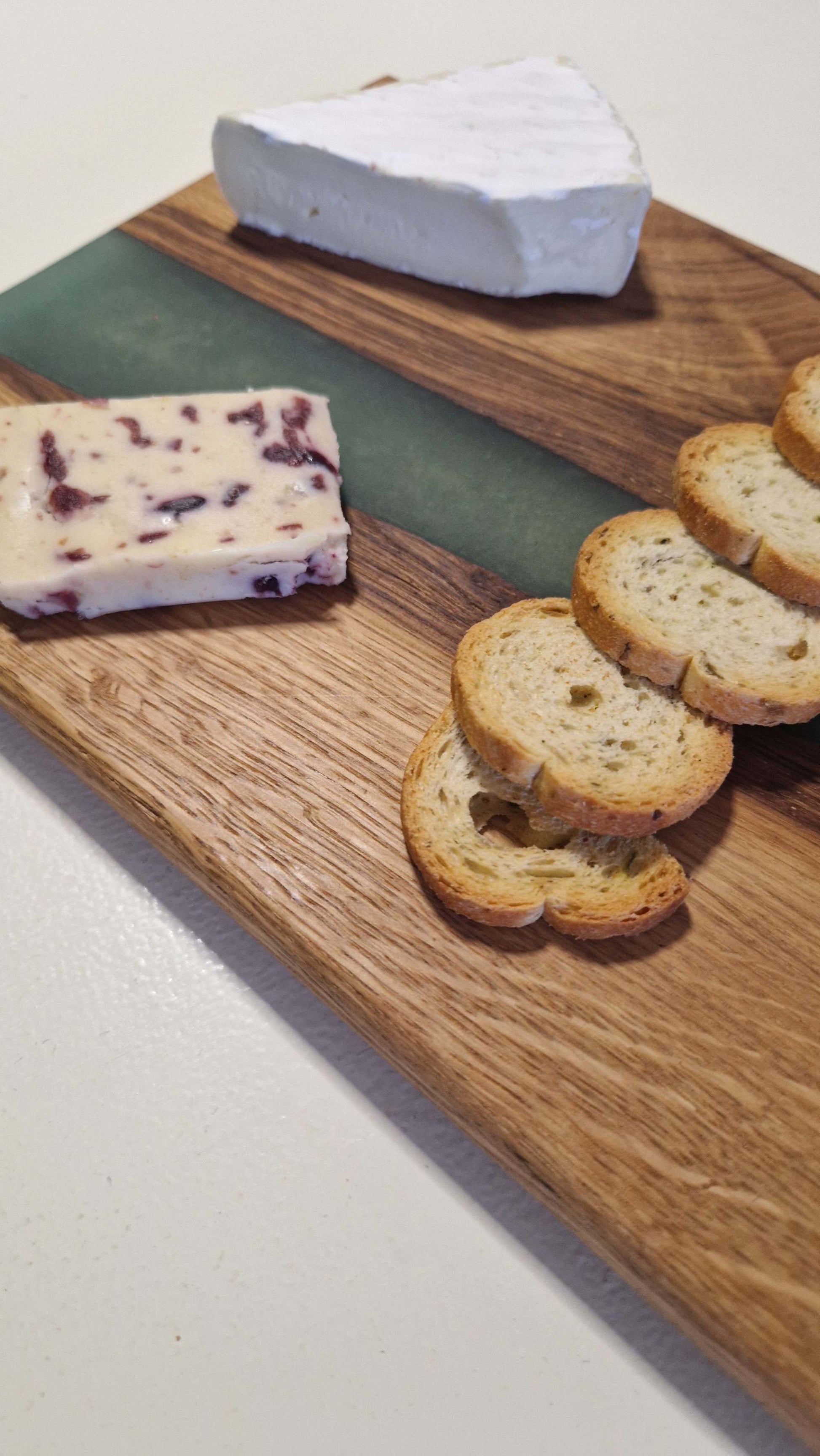 Handmade oak charcuterie and cheese board with green epoxy, featuring assorted cheese and crackers.