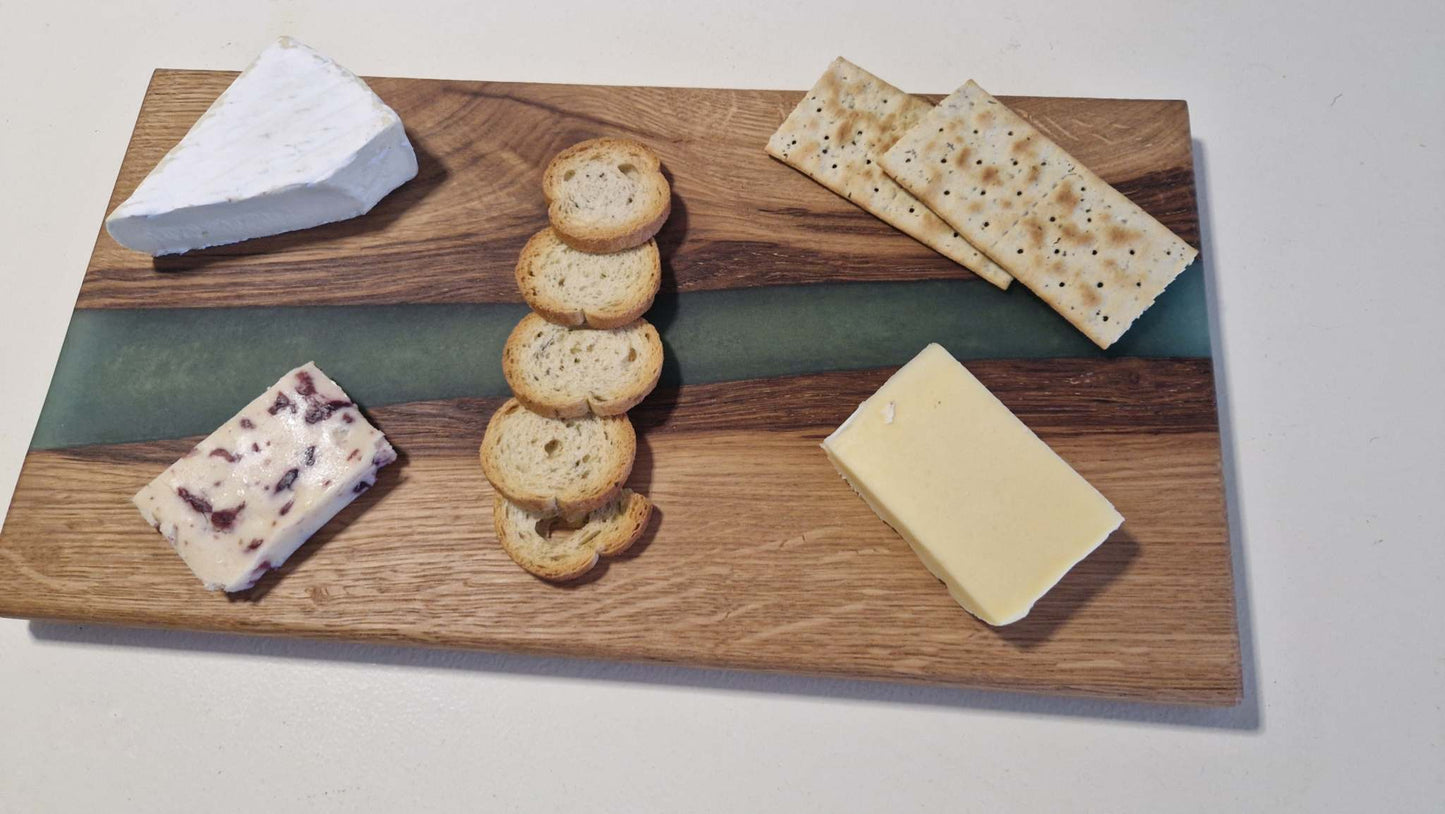 Handmade charcuterie board in oak with green epoxy, featuring cheeses and crackers.