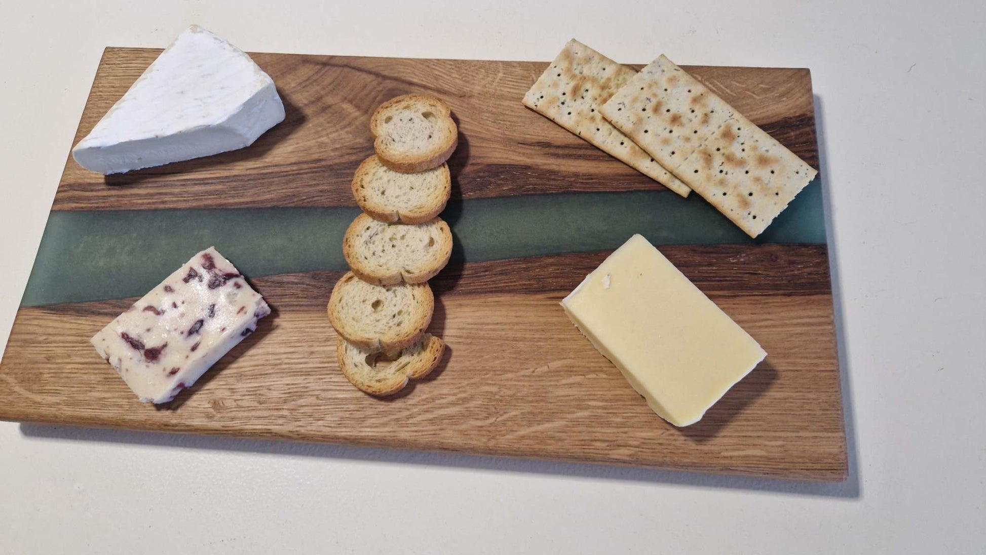 Handmade charcuterie board in oak with green epoxy, featuring cheeses and crackers.