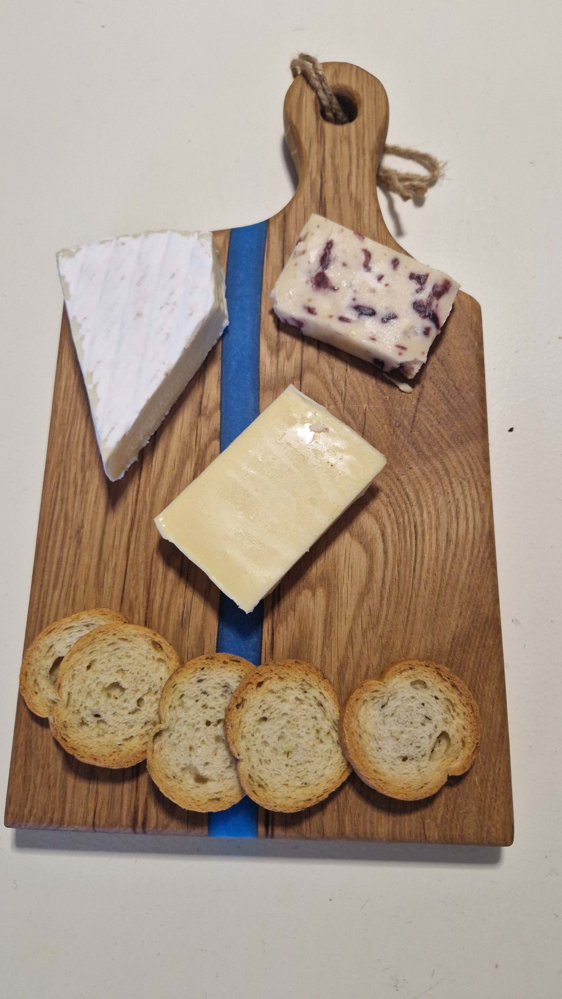Handmade charcuterie board with blue epoxy, oak wood, cheese and crackers.