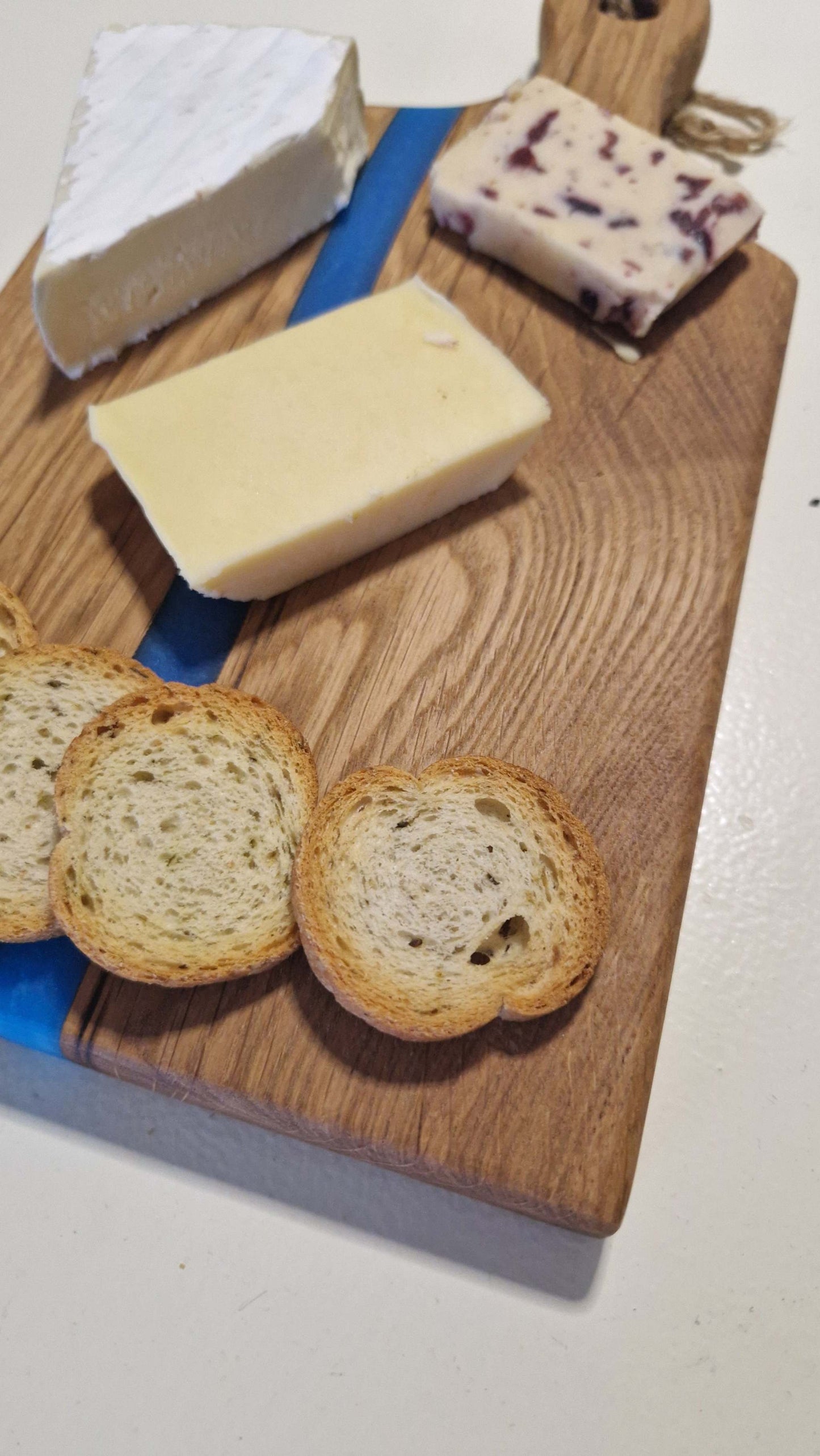Handmade oak charcuterie and cheese board with blue epoxy design, featuring assorted cheeses and crackers.