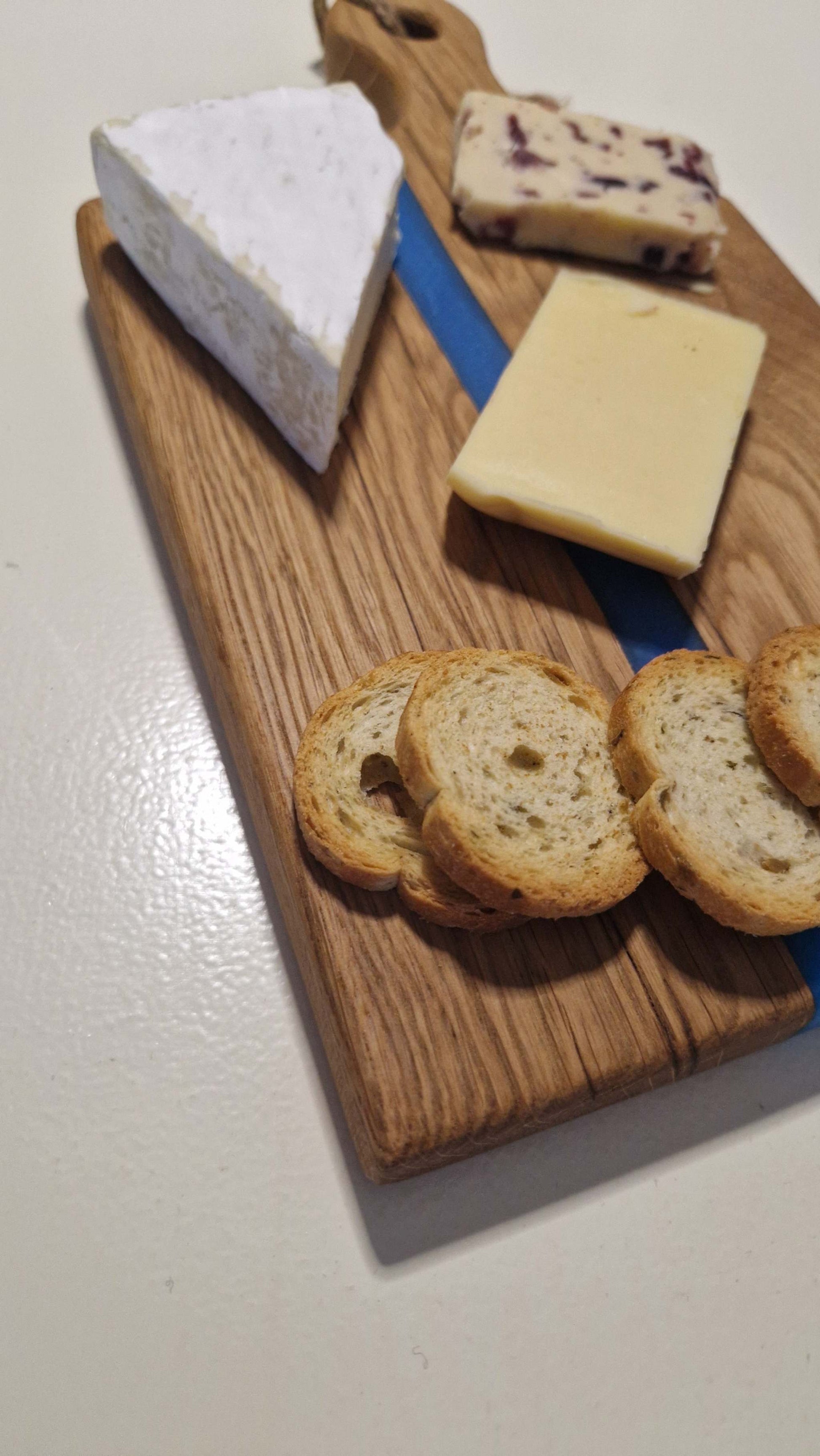 Handmade charcuterie board with blue epoxy stripe displaying assorted cheeses and crackers.