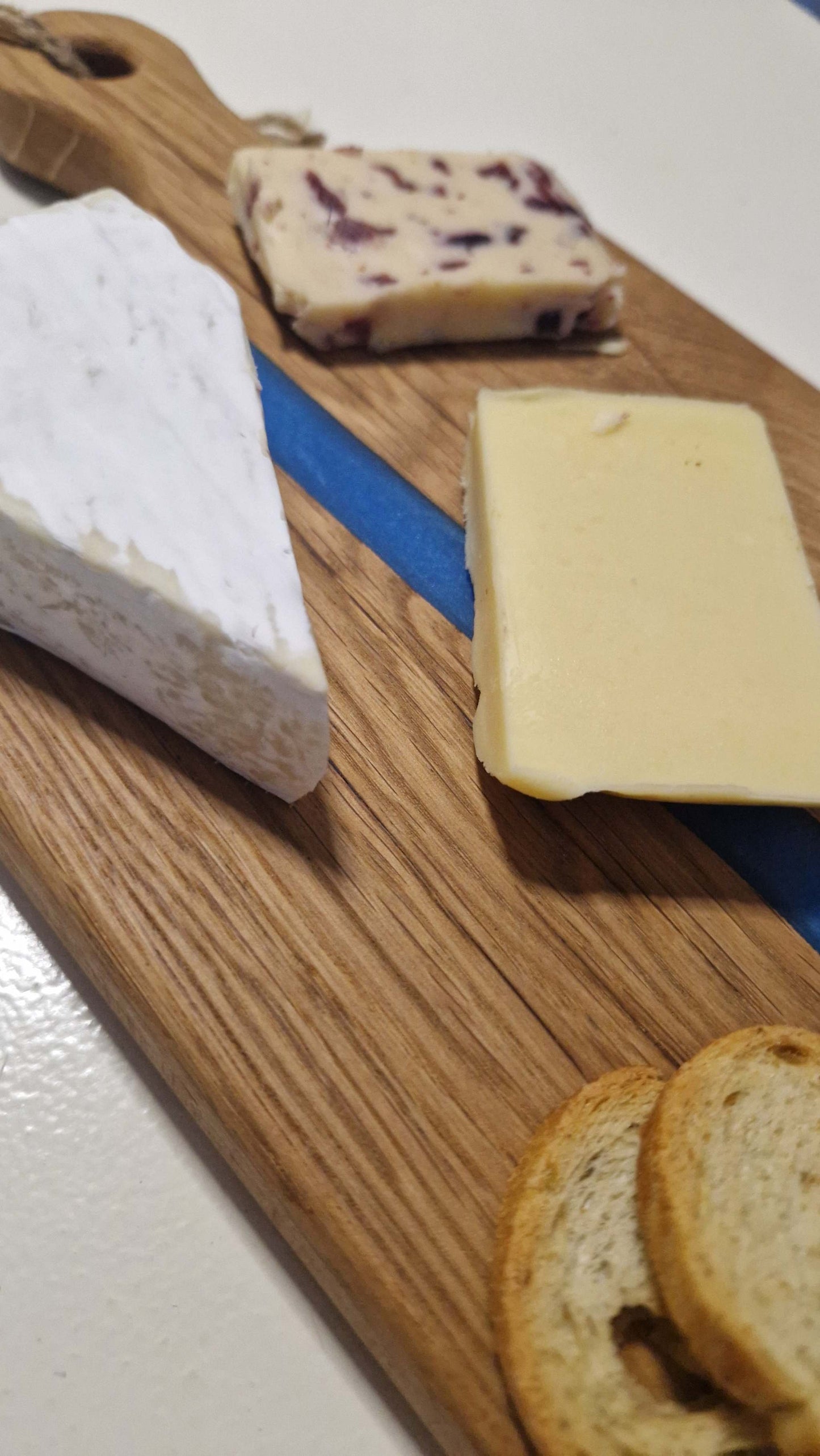 Handmade charcuterie board with blue epoxy and cheese assortment.