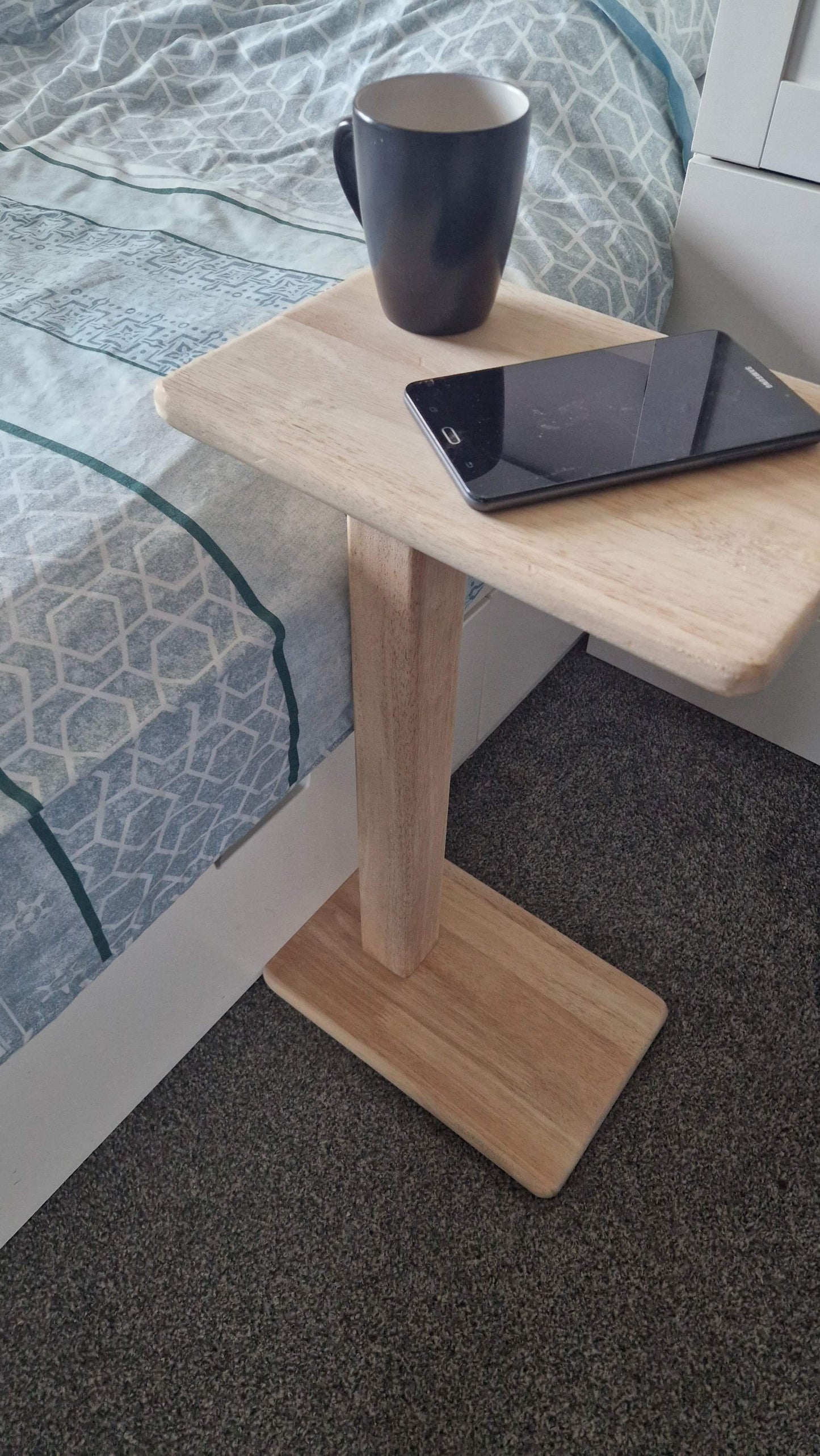 Handmade oak wooden couch table next to bed with cup and smartphone placed on top.