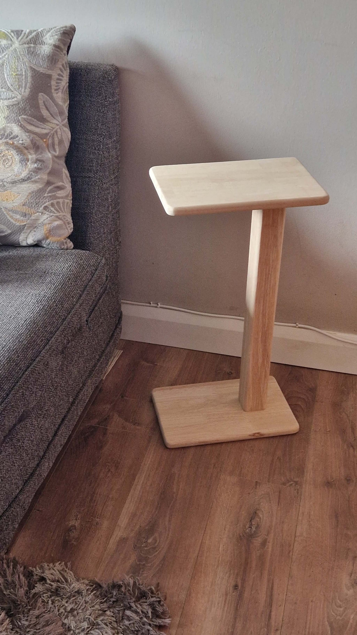 Handmade oak wooden couch table with sleek C-shape, beside a grey sofa.
