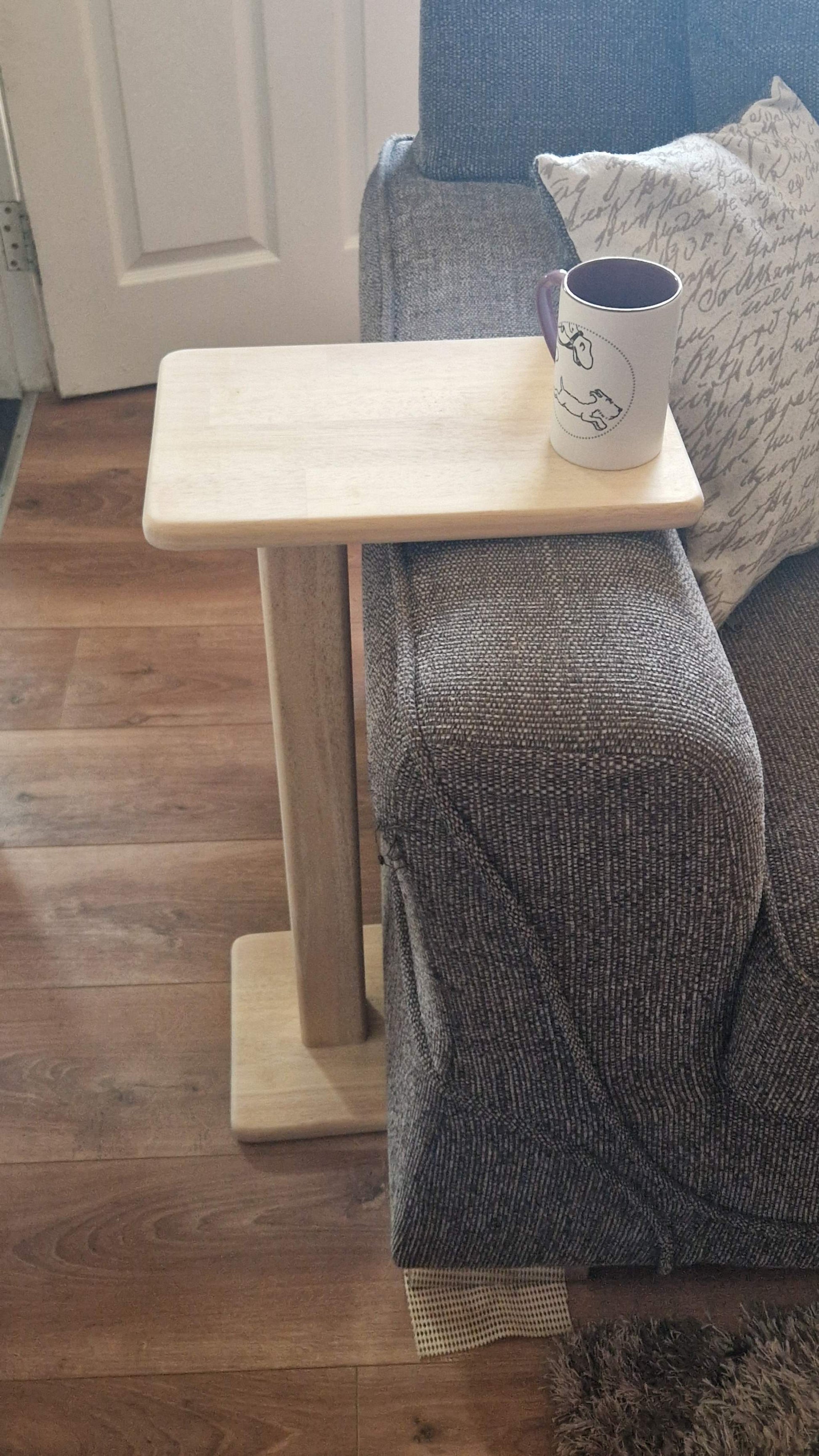 Handmade oak wooden couch table with sleek C-shape design, placed beside a sofa with a mug on top.