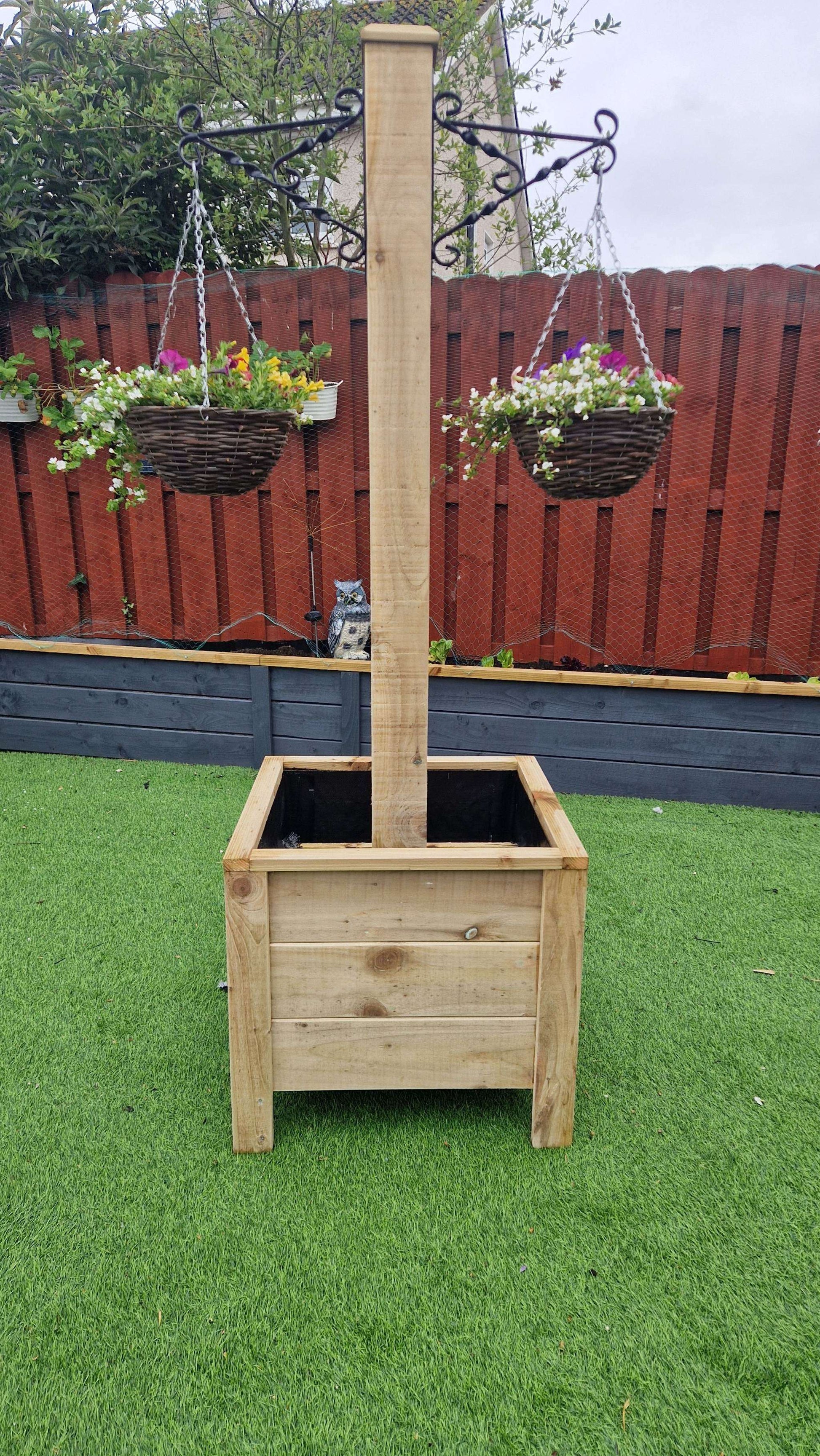 Handcrafted wooden planter with integrated hanging basket pole on a green garden lawn.