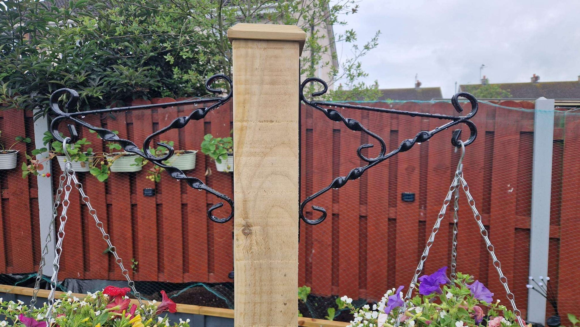 Handcrafted wooden planter with integrated hanging basket pole on a green garden lawn.